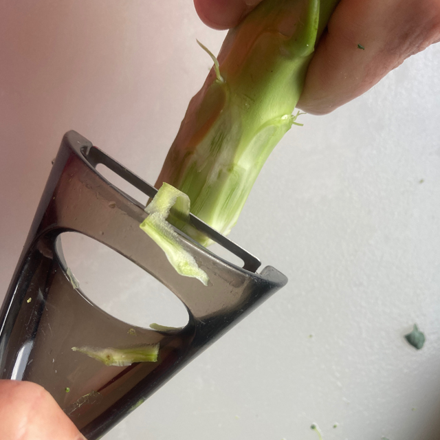 Broccoli stalk being peeled with a vegetable peeler.