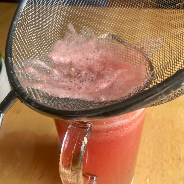 Straining the watermelon mixture into a glass.