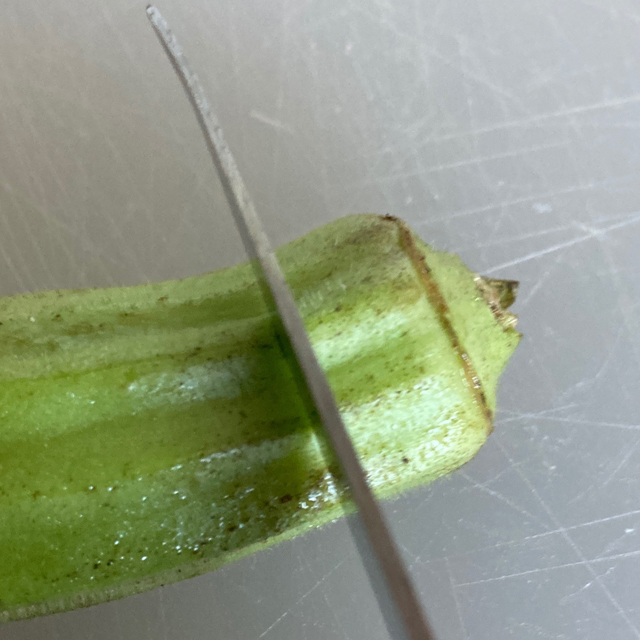 Okra being cut with a knife.