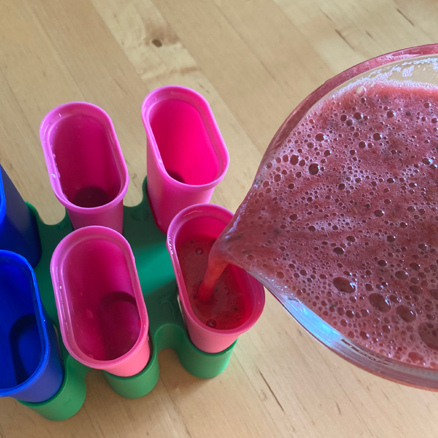 Pouring the blended fruit into the popsicle molds.