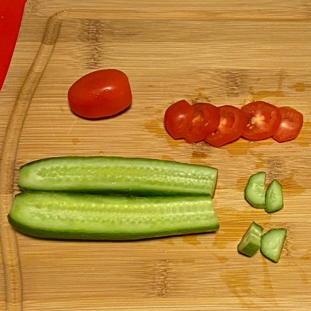 Cucumber and tomatoes sliced on a cutting board.