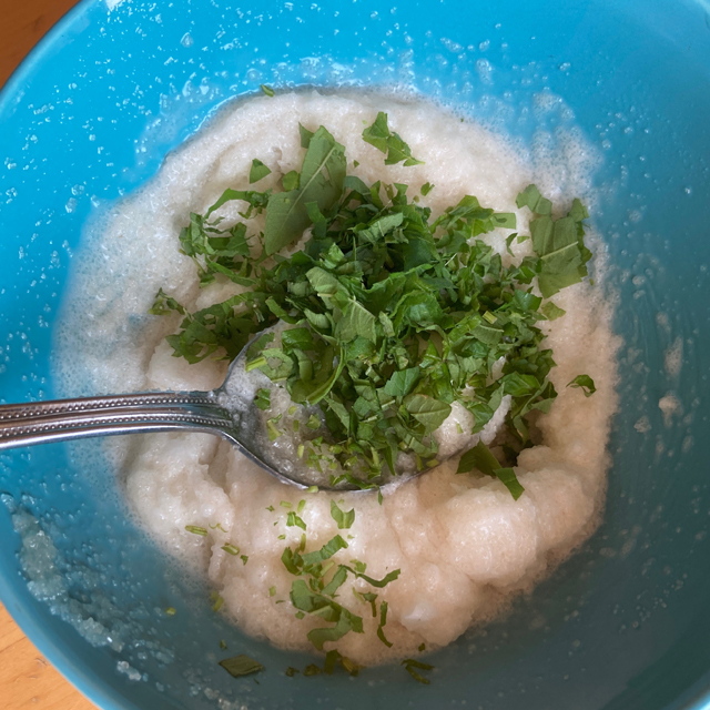 Sugar, coconut oil, and herbs in a bowl being mixed with a spoon.