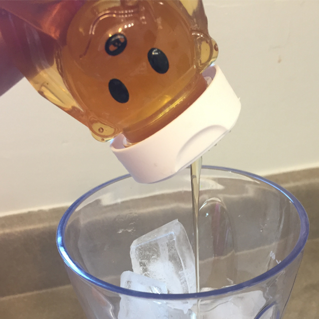 Honey being squeezed into a blender with ice and juice.
