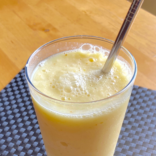 Finished citrus smoothie in a glass with a straw.
