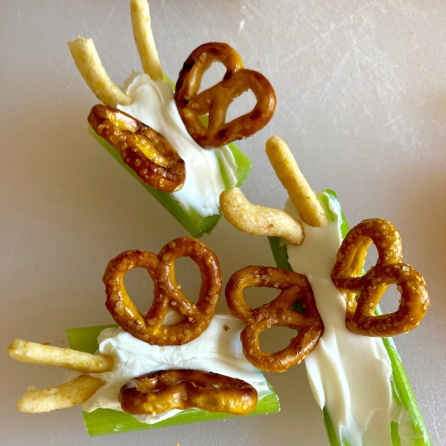 Celery with cream cheese and pretzels, resembling an insect with wings.