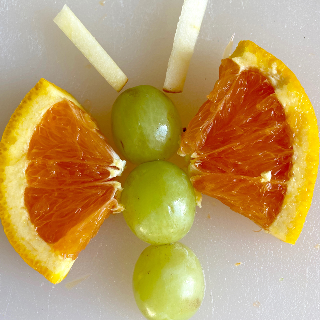 Orange pieces and grapes arranged to look like an insect.