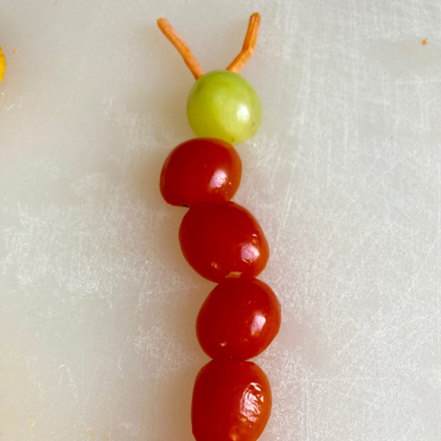cherry tomatoes, carrot, and grapes arranged to look like a caterpillar.